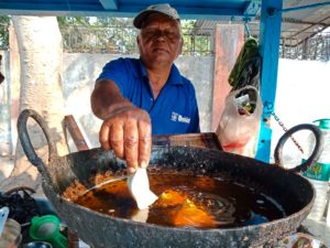 man dropping dough into large pan of oil