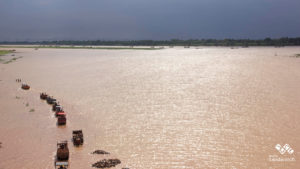 line of tractors loading sand in shallow part of wide river