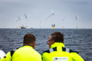 Dos personas con camperas verdes miran hacia el Parque eólico Hollandse Kust Zuid, en el Mar del Norte