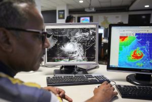 A man looks at two computer screens displaying weather patterns, office environment